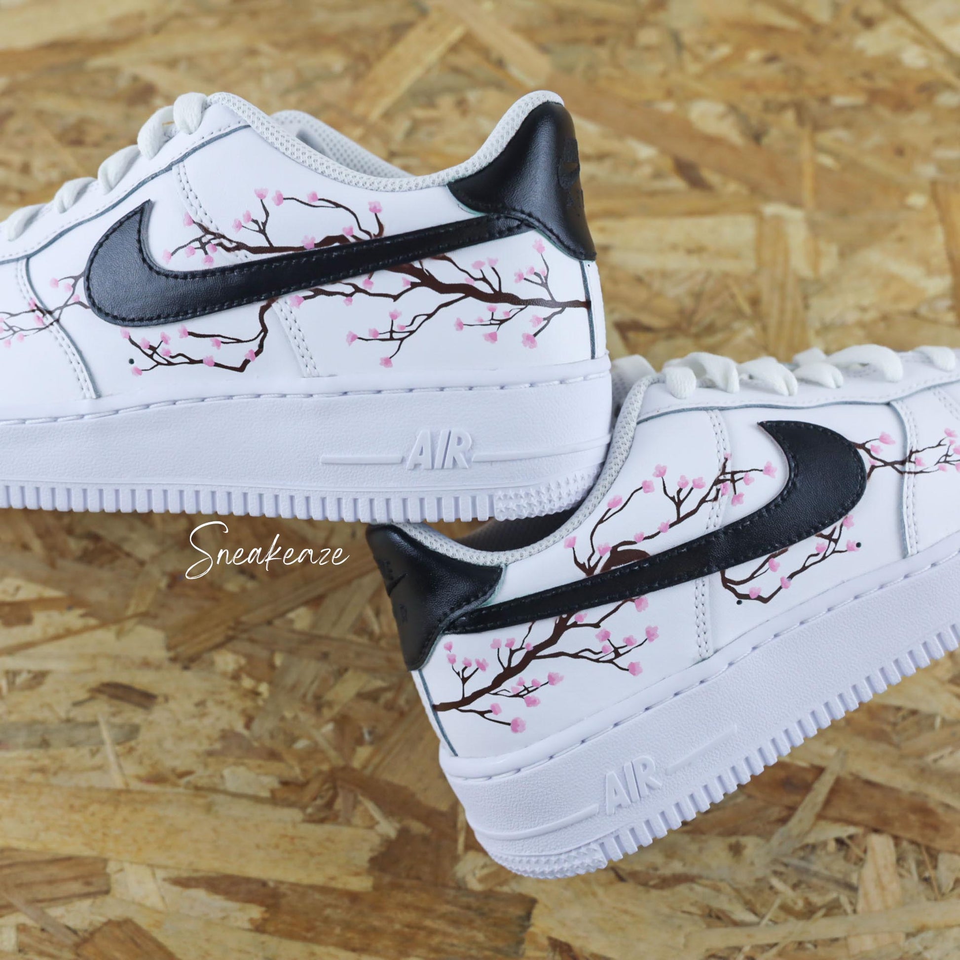 Baskets Air Force 1 custom cherry blossom avec swoosh et talon peint en noir et dessin fleurs de cerisiers peint à la main sur les côtés extérieurs uniquement couleur rose pastel.