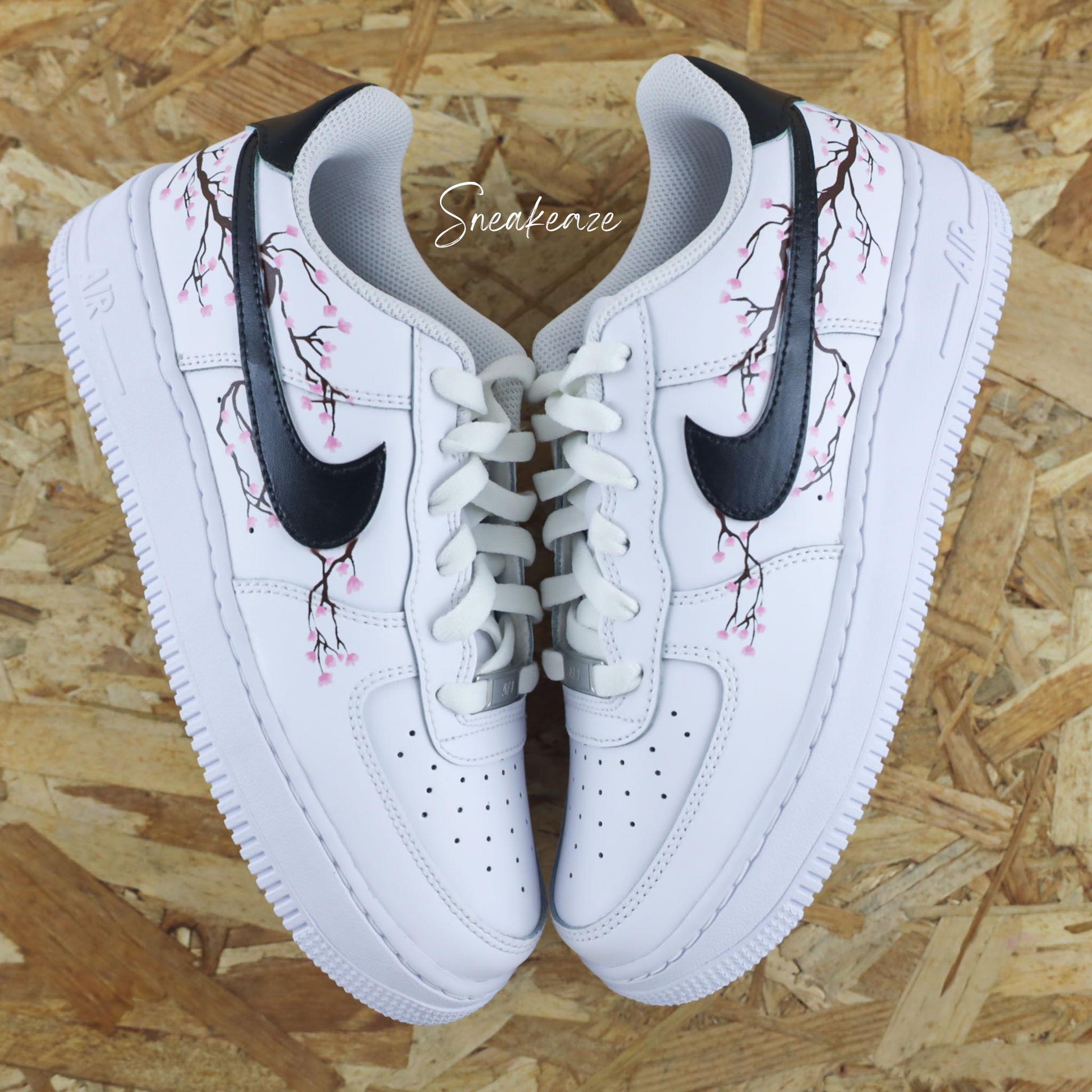 Baskets Air Force 1 custom cherry blossom avec swoosh et talon peint en noir et dessin fleurs de cerisiers peint à la main sur les côtés extérieurs uniquement couleur rose pastel.