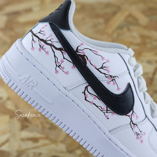 Baskets Air Force 1 custom cherry blossom avec swoosh et talon peint en noir et dessin fleurs de cerisiers peint à la main sur les côtés extérieurs uniquement couleur rose pastel.