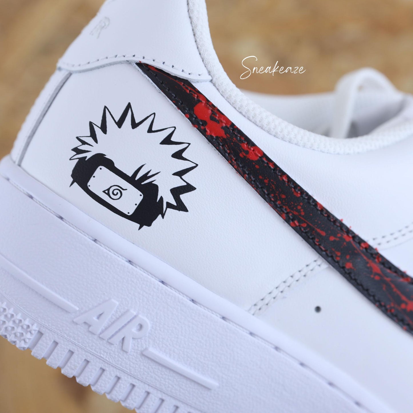 Nike Air Force 1 custom avec motifs Naruto sur les côtés extérieurs, swoosh noir et splash rouge intense — une paire unique pour les fans de manga et de sneakers.