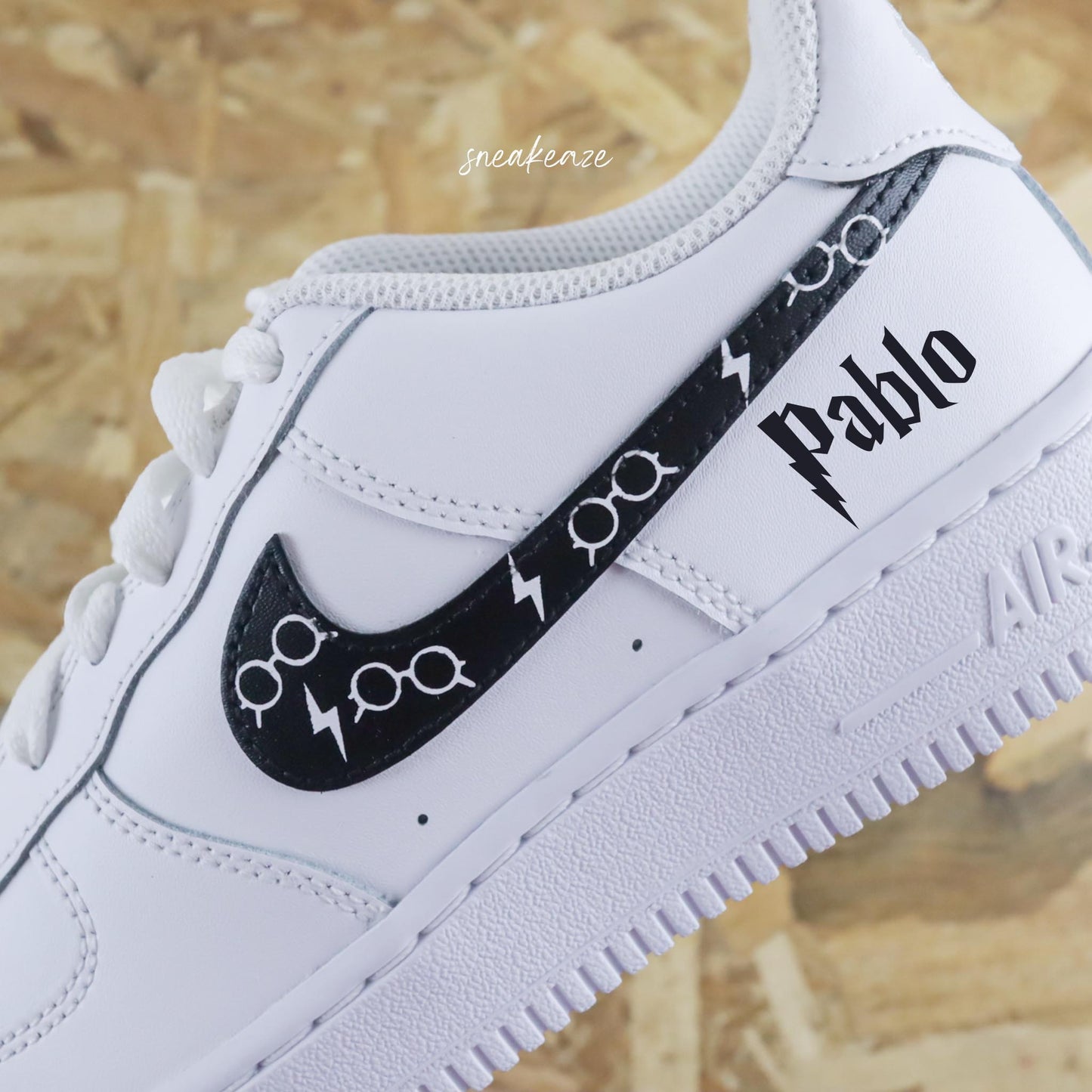 Basket Nike air force one custom modèle harry potter. Les 4 signes Nike sont peints en noir avec dessin de lunettes inscription du prénom sneakeaze custom