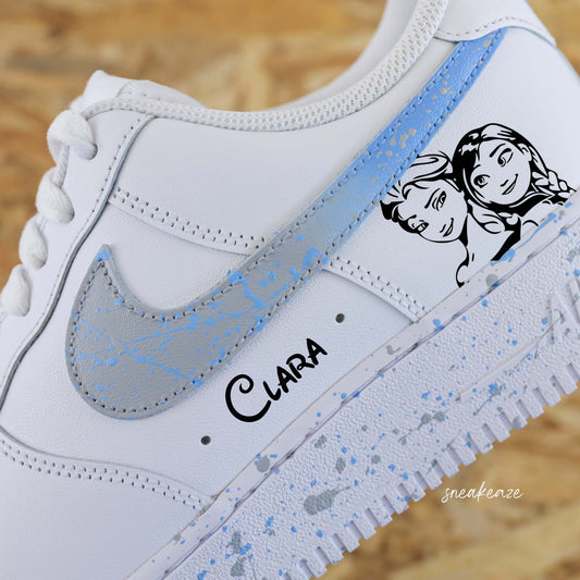Baskets Nike Air Force 1 custom splash dégradé gris et bleu clair avec dessin d'Elsa et Anna de la reine des neiges. Inscription du prénom sous le swoosh.