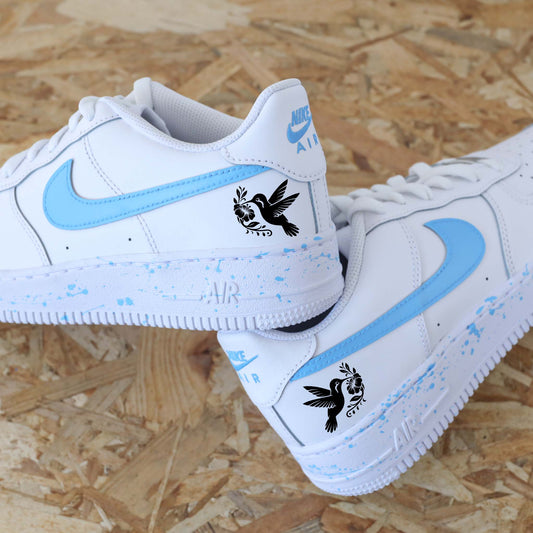 Baskets Nike Air Force 1 custom modèle swoosh bleu azur et splash assortis sur les semelles + dessin d'un colibri sur les côtés extérieurs.