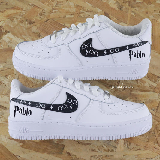 Basket Nike air force one custom modèle harry potter. Les 4 signes Nike sont peints en noir avec dessin de lunettes inscription du prénom sneakeaze custom