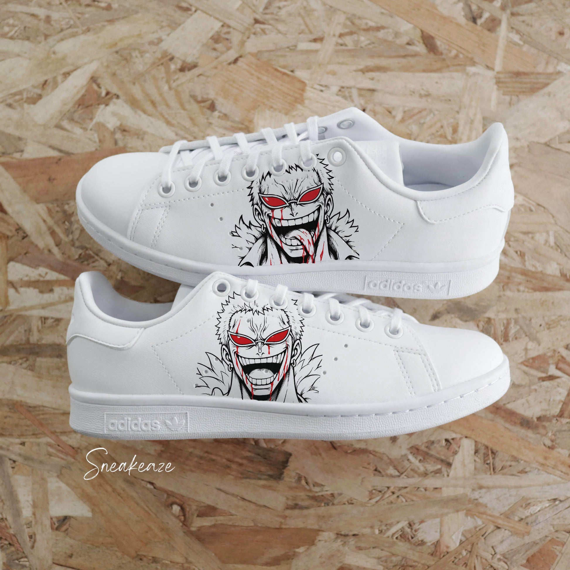 Paires d'Adidas Stan Smith blanches customisées à la main par Sneakeaze Customs avec le portrait de Doflamingo de One Piece.