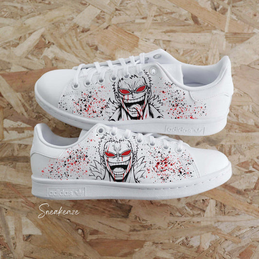 Paires d'Adidas Stan Smith blanches customisées à la main par Sneakeaze Customs avec le portrait de Doflamingo de One Piece.