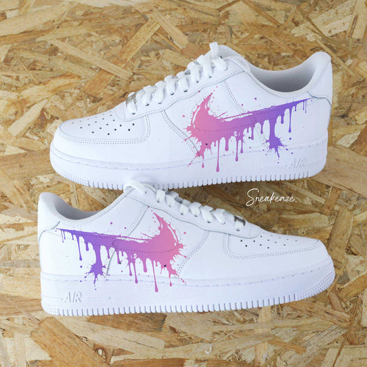 Paires de Nike Air Force 1 blanches customisées à la main par Sneakeaze Customs avec un effet Swoosh coulant en dégradé rose et violet.