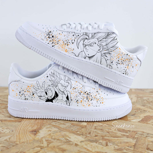 Paires de Nike Air Force 1 blanches customisées par Sneakeaze Customs avec le portrait de Gogeta de Dragon Ball Z et des éclaboussures de peinture orange et noire.